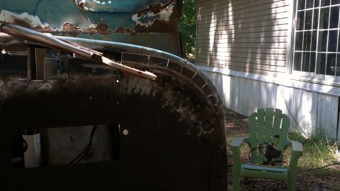 1978 Ford Bronco - This image shows a partially restored vehicle fender, with visible rust and ongoing metalwork, set against a backdrop of a house and yard.