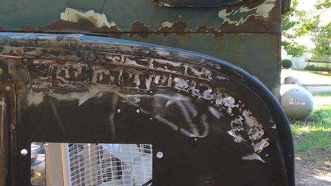 1978 Ford Bronco - Close-up of a rusty and repaired vehicle body panel, with a fan and propane tank visible.