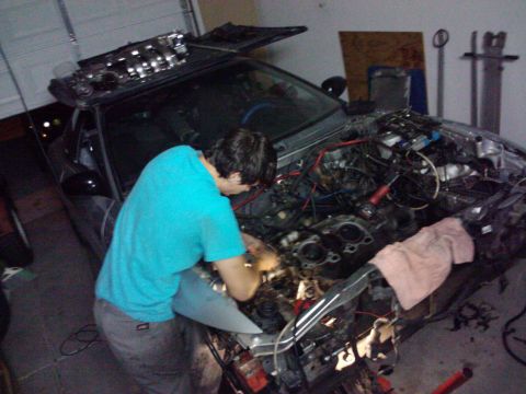 1995 Ford Probe - A person is actively working on the engine of a car, with the hood fully open and components exposed.