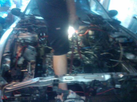 1995 Ford Probe - A person works on the complex engine of a car, with many wires and parts exposed.