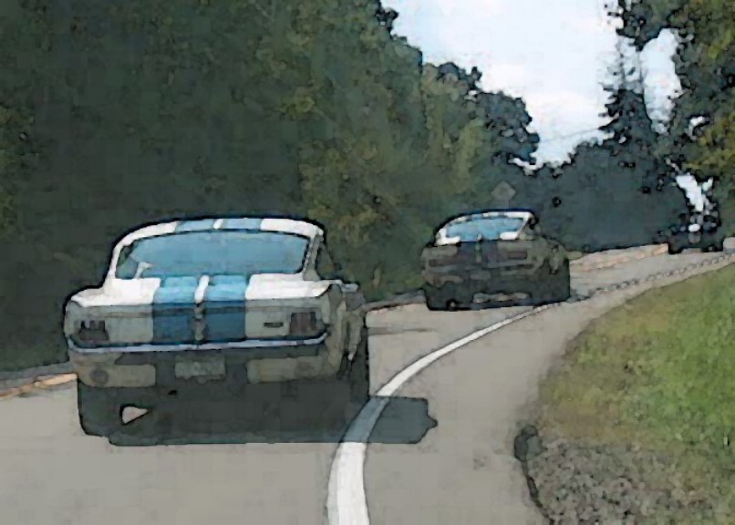 White 1965 Ford Mustang coupe with blue stripes, rear view, on a road with another car