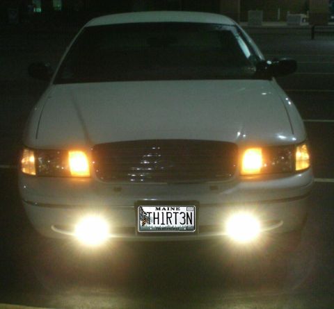 1998 Ford Crown Victoria - A white sedan is seen from the front at night, with its headlights and fog lights illuminated.