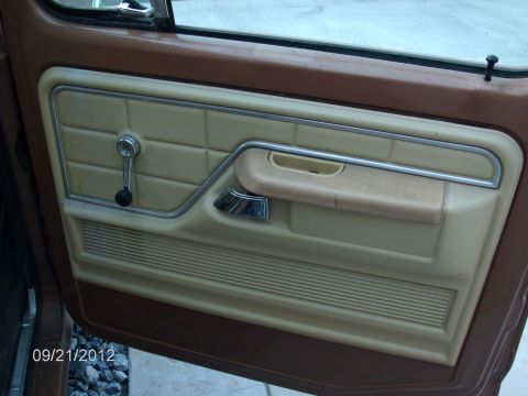 1979 Ford F-150 - The interior door panel of a 1979 Ford F-150 features tan upholstery with a chrome trim and window crank.