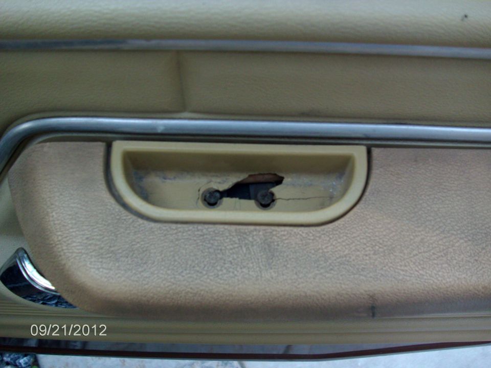 Close-up of a tan car door panel with a damaged pull handle and visible screws