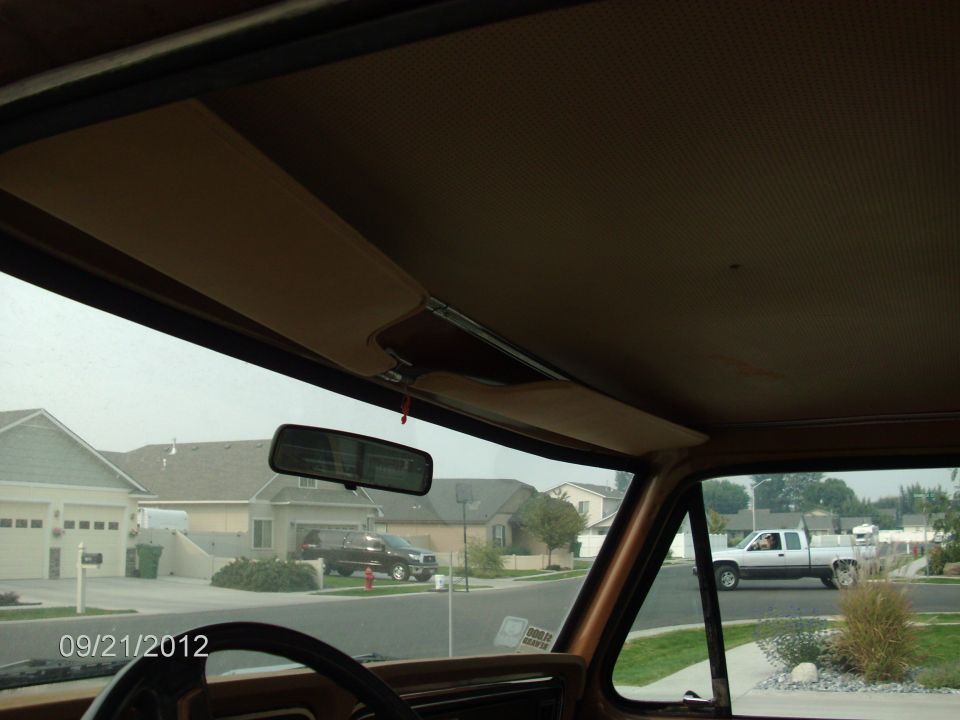 View from inside a truck, looking out at a suburban street with houses and another truck driving by. The interior shows the headliner and rearview mirror