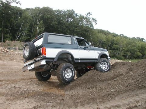 1994 Ford Bronco - 1994 Ford Bronco shown off-road, navigating a dirt incline with its spare tire mounted externally.