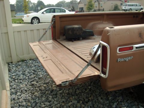 1979 Ford F-150 - The tailgate of a brown 1979 Ford F-150 Ranger pickup truck is open, revealing the truck bed and a black component.