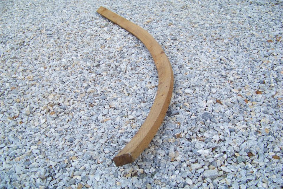 Curved wooden piece lying on a bed of light gray gravel. A watermark reads 'SUPER MOTORS'