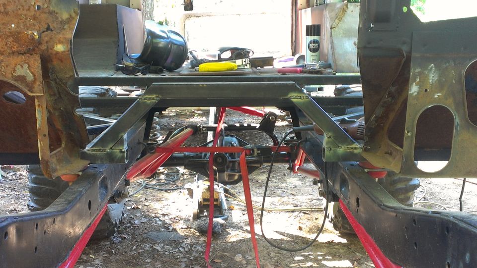 Vehicle frame and suspension components, possibly undergoing repair or modification. Red straps and metal supports are visible
