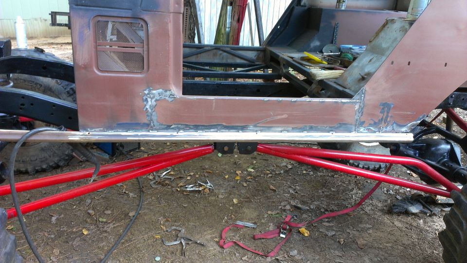 Off-road vehicle frame with red suspension components and body panels undergoing repair