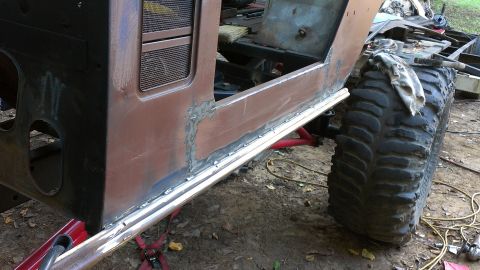 1978 Ford Bronco - The body of a vehicle is being worked on, with visible welding along the rocker panel and a massive tire attached.