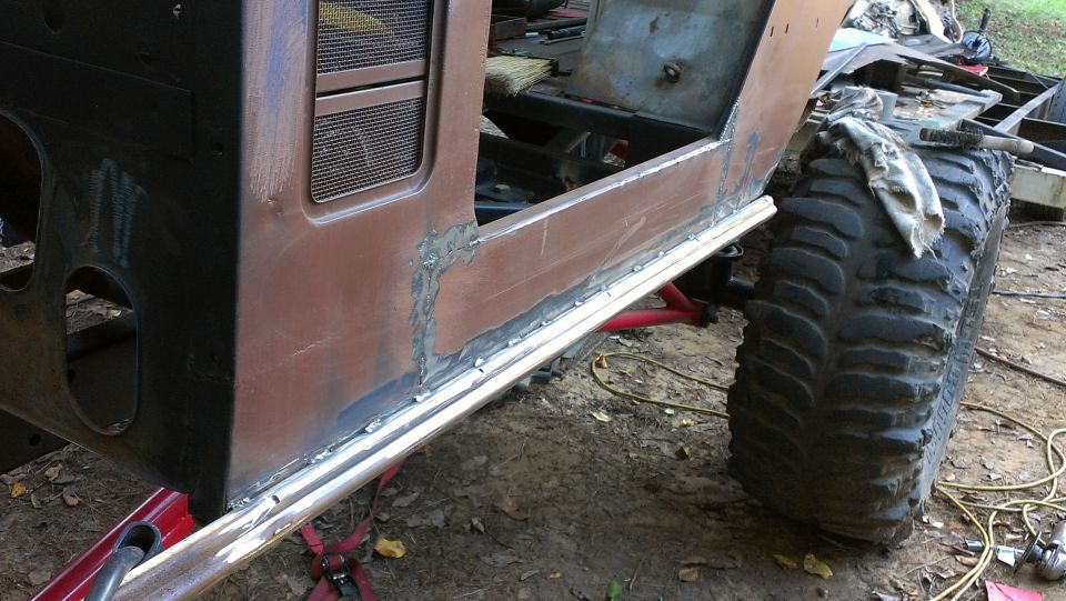 Side panel of a vehicle undergoing repair, showing welding work and a large off-road tire