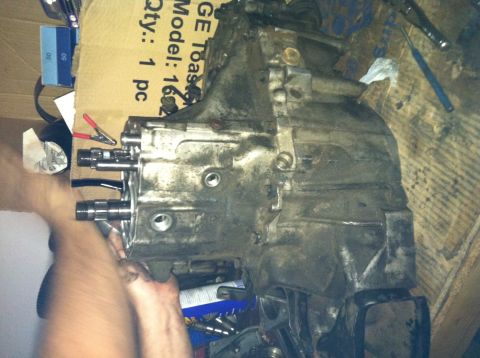 1993 Ford Probe - Transmission assembly with visible shafts and bolts, partially obscured by hands. Cardboard box in background.