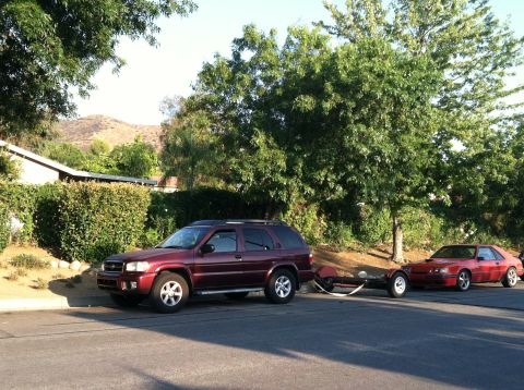 1993 Ford Probe - Maroon SUV tows a trailer carrying a red sports car on a sunny day.