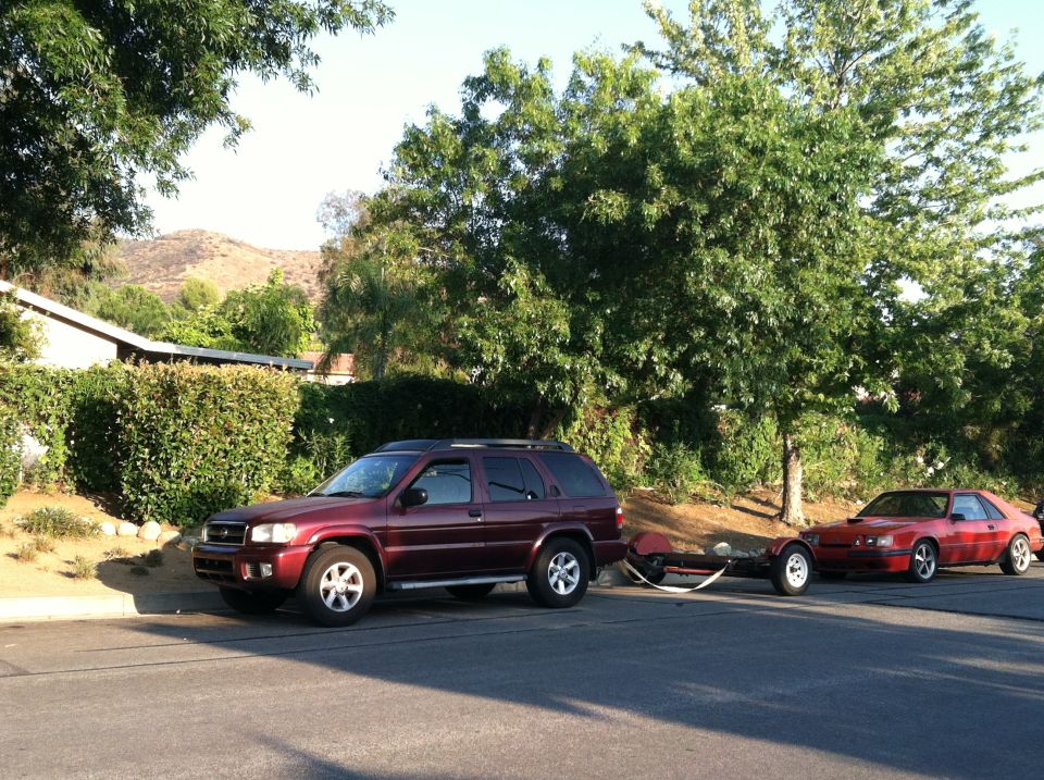 Maroon SUV towing a trailer with a red sports car. Supermotors.net logo visible