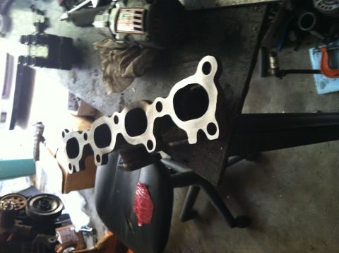 1993 Ford Probe - An exhaust manifold sits on a table, surrounded by various engine components and tools.