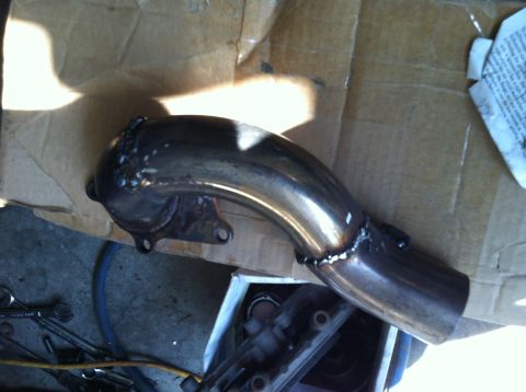 1993 Ford Probe - A metal exhaust pipe is shown, with visible welds and mounting points, on a surface with tools and cardboard.