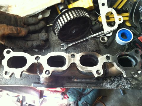 1993 Ford Probe - Close-up of an exhaust manifold and various engine components laid out on a cluttered workbench.