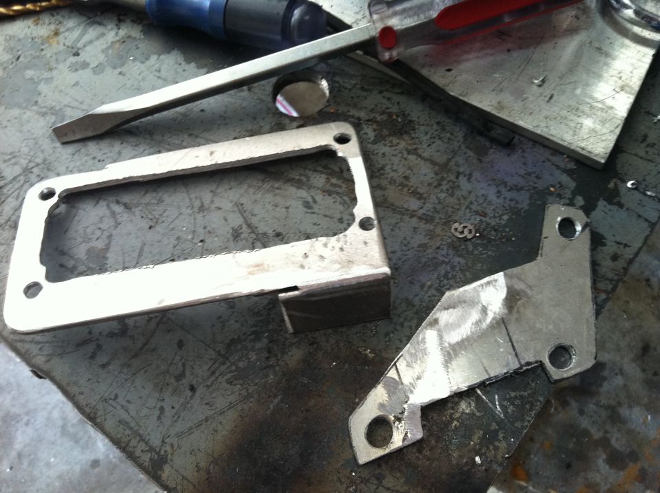 Metal bracket and frame parts on a workbench with a screwdriver and chisel