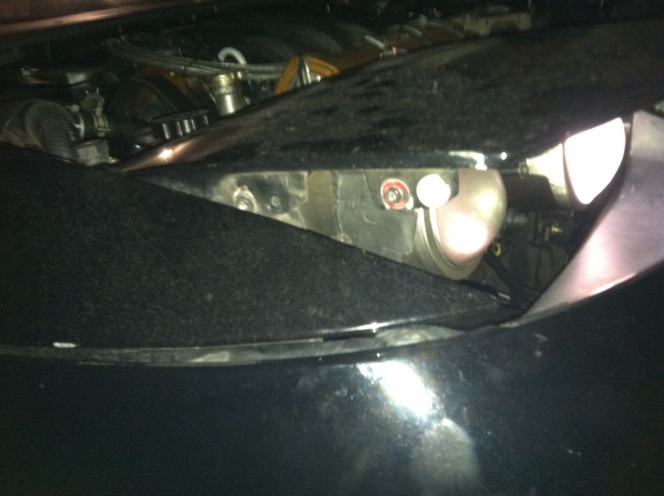 Close-up of a car's headlight assembly, showing the bulb housing and surrounding black textured material