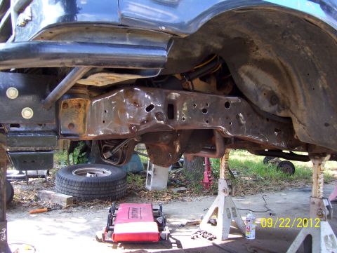 1990 Ford Bronco - Vehicle frame and suspension components are visible while the vehicle is supported by jack stands, with a spare tire nearby.