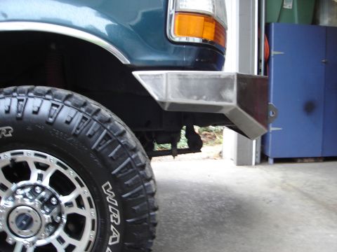 1989 Ford Bronco - A custom metal bumper is installed on the front of a teal Ford truck, with a large tire in the foreground.