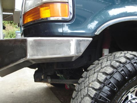 1989 Ford Bronco - Close-up view of a custom metal front bumper and a large off-road tire on a dark-colored vehicle.