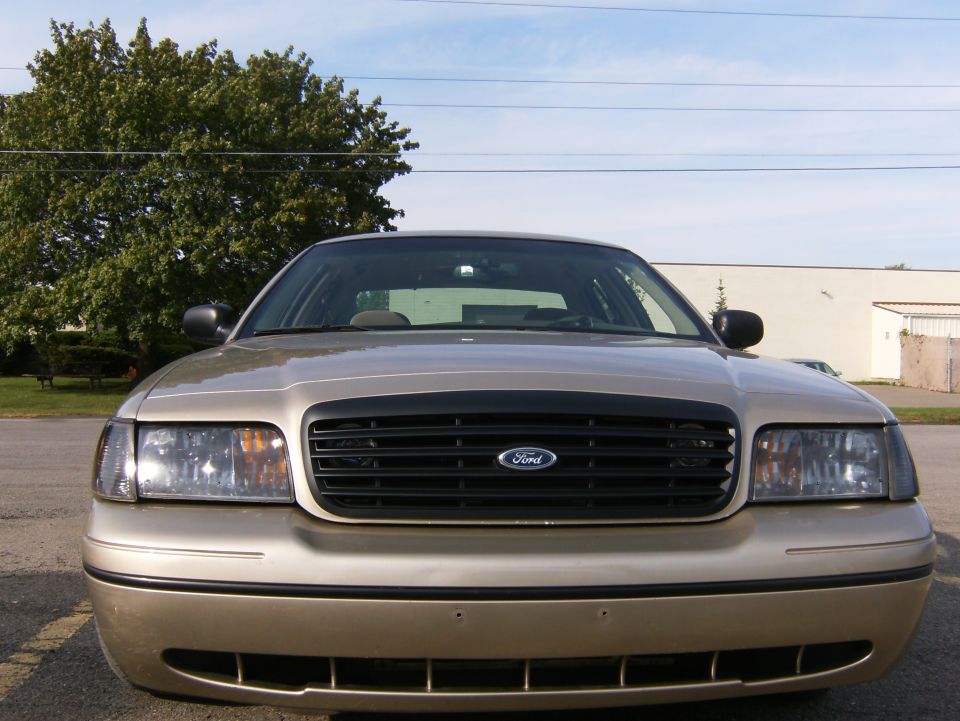 Front view of a tan Ford Crown Victoria sedan with blue oval grille emblem outdoors