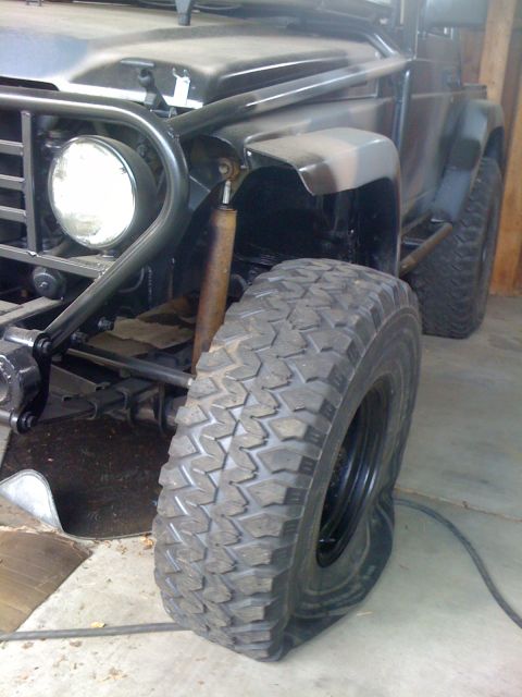 1987 Suzuki Samurai - A dark-colored off-road vehicle with a flat tire and visible roll cage is parked indoors.