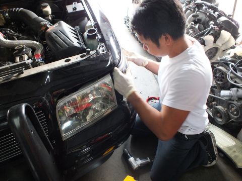 2003 Ford Crown Victoria - Mechanic in latex gloves works on the front headlight area of a black vehicle in a shop.