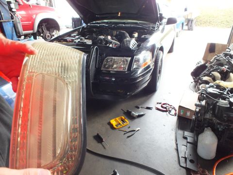 2003 Ford Crown Victoria - Worker holds a smoked tail light while a black sedan sits in a shop with a spare engine nearby.