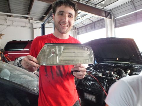 2003 Ford Crown Victoria - Man in a red shirt grins while holding a clear corner lamp lens in a garage with cars behind.