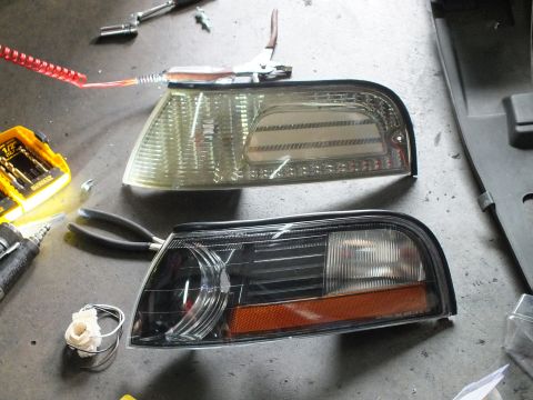 2003 Ford Crown Victoria - Two front corner marker lamps laid on the floor, comparing a clear lens to a black-housing version.