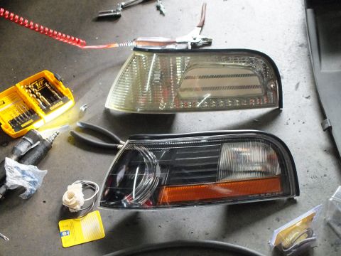 2003 Ford Crown Victoria - Pair of front corner marker lamps, one clear and one black-housing, displayed near a drill set.
