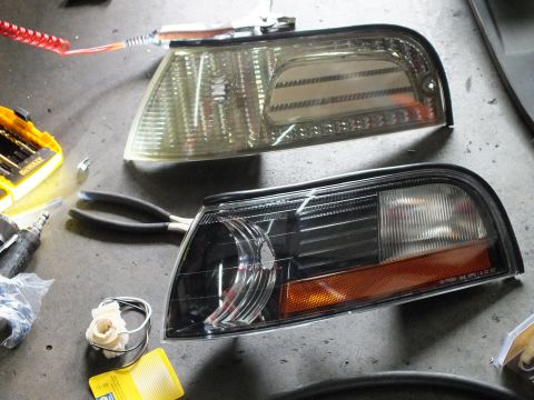 2003 Ford Crown Victoria - Pair of replacement front corner lamp assemblies laid on shop floor next to a Dewalt bit set and pliers during install