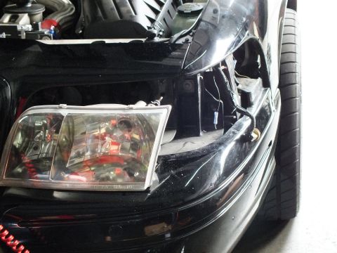 2003 Ford Crown Victoria - Headlight pulled from black sedan front end, harness and mounting bracket visible during corner lamp swap