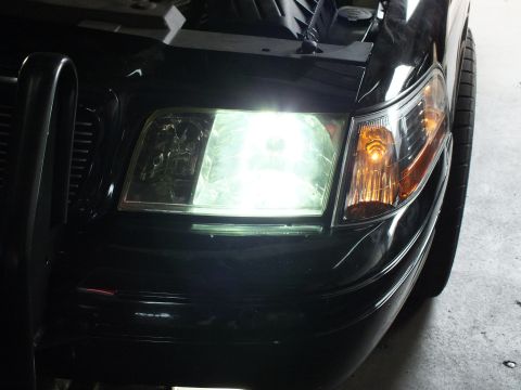 2003 Ford Crown Victoria - Illuminated white headlight and amber corner lamp on a black vehicle front end inside a garage