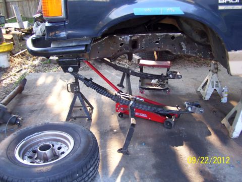 1990 Ford Bronco - The frame of a Ford Bronco is undergoing repairs, supported by jack stands and a hydraulic jack.