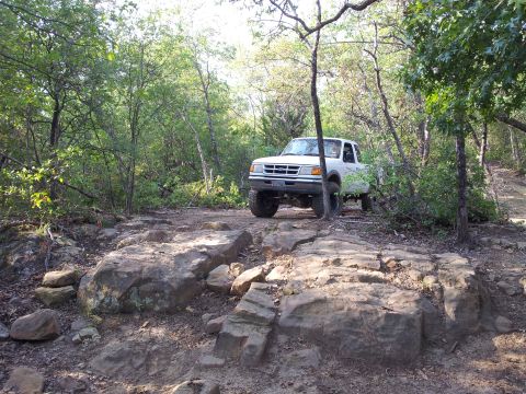 1994 Ford Ranger - A white Ford Ranger navigates a challenging off-road path through a wooded area.