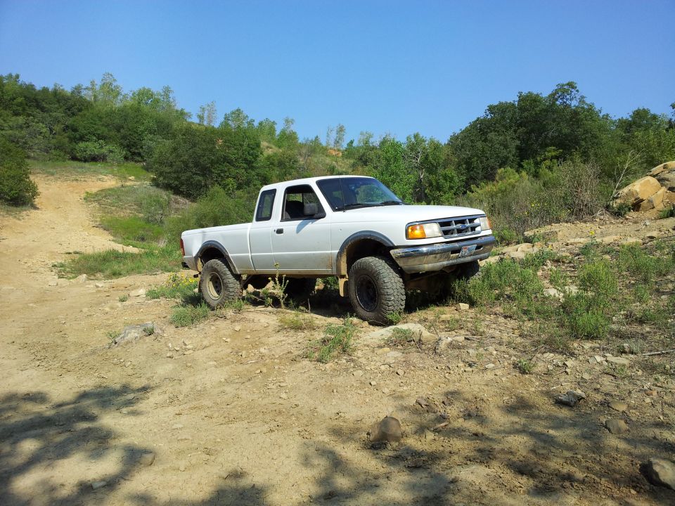 White Ford Ranger pickup truck on a dirt road, front 3/4 view, lifted suspension, off-road tires