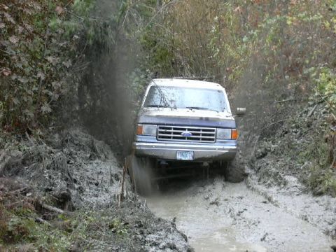 1988 Ford Bronco - A Ford truck navigates a muddy trail, its grille suggesting a late 1980s model year.