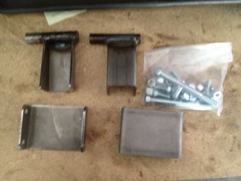 1965 Ford Mustang - Four metal brackets and a bag of assorted bolts and nuts are laid out on a textured surface.