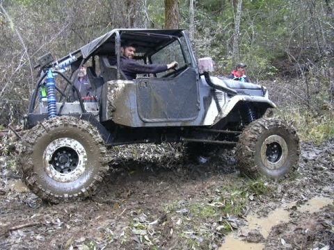1988 Ford Bronco - Modified off-road vehicle navigates a muddy trail with two occupants.