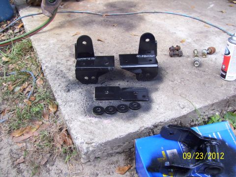 1990 Ford Bronco - Black metal brackets and hardware are laid out on a concrete surface next to a spray can and a blue box with a date stamp.