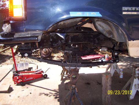 1990 Ford Bronco - The rear leaf springs and suspension components of a Ford Bronco are being worked on, with the vehicle supported by jack stands.