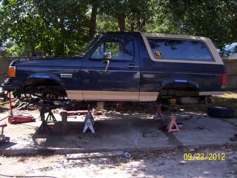 1990 Ford Bronco - A 1990 Ford Bronco is lifted on jack stands in a driveway, with tools scattered around.
