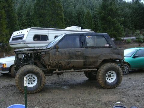 1988 Ford Bronco - This heavily modified SUV is covered in mud, suggesting recent off-road use, and is parked near a camper and another vehicle.