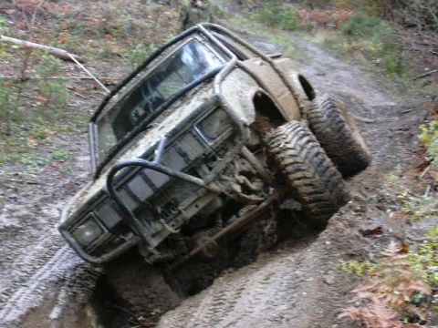 1988 Ford Bronco - This heavily modified off-road vehicle is navigating a steep, muddy trail, demonstrating its off-road capabilities.