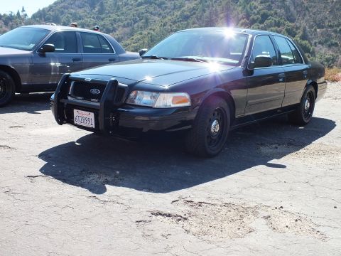 2003 Ford Crown Victoria - Black Ford Crown Victoria police-style sedan with push bar and steel wheels at a hillside turnout