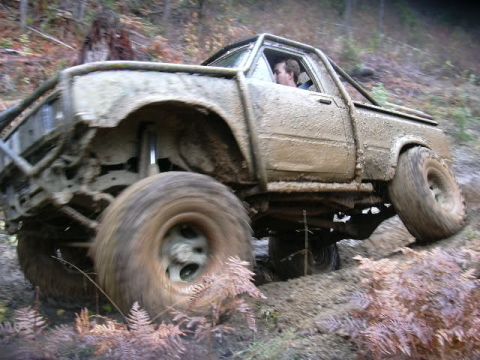 1988 Ford Bronco - This heavily modified pickup truck is shown tackling a challenging off-road course covered in mud.
